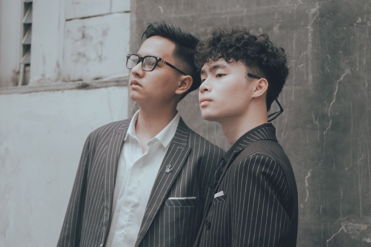 services-02 Two Asian men in striped suits and eyewear posing outdoors in Hanoi, Vietnam.