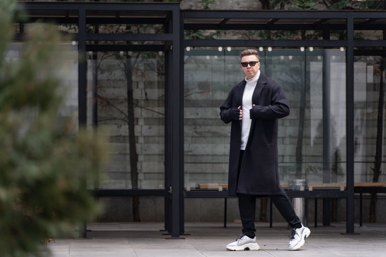 services-03 Fashionable man in sunglasses and long coat standing confidently in urban setting.