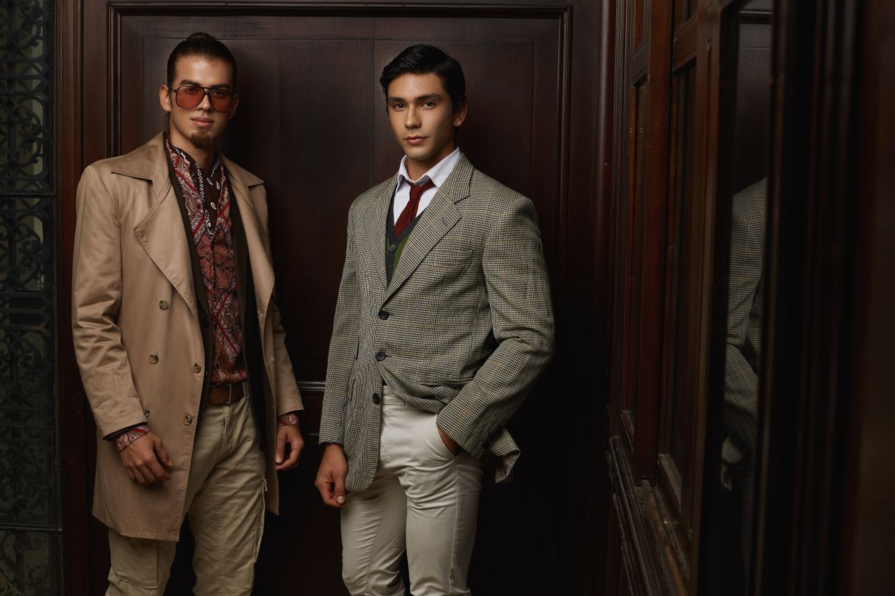 services-01 Two men in fashionable suits posing indoors, showcasing elegance and style.
